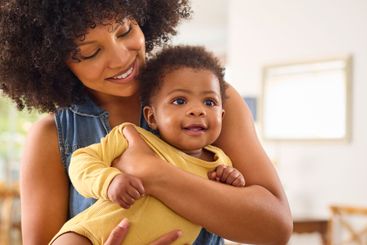 Loving Mother Indoors At Home Standing Cuddling Baby...