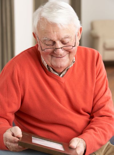 Senior Man Looking At Photograph In Frame