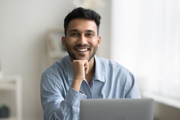 Portrait happy smiling young man sitting at workplace by...