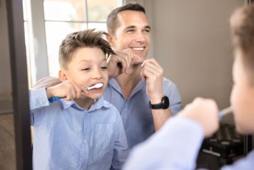 Cheerful dad and sweet son kid brushing teeth together