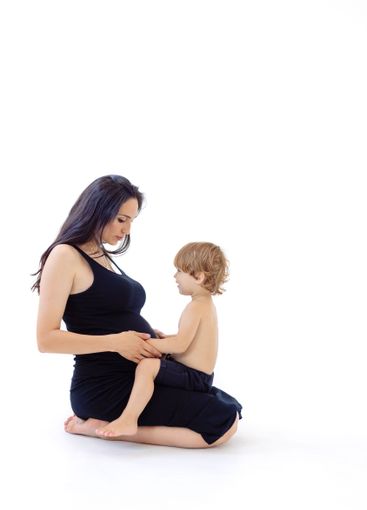 A young pregnant woman in a black dress is sitting on...