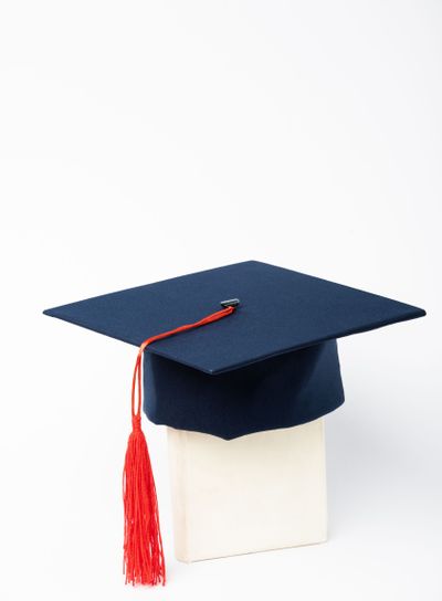 Blue graduation cap with red tassel on book on white...