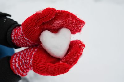 red female gloves hold a white heart from the snow