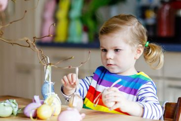 Cute little toddler girl decorating tree bough with...