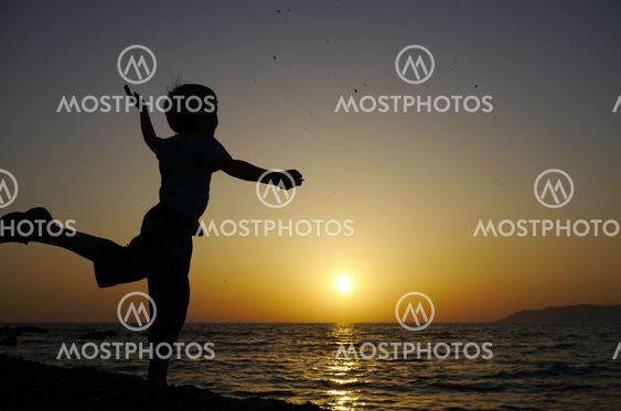 young boy throws stones into the ocean