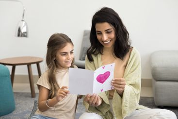 Cute little daughter presenting to mommy lovely postcard...