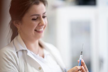 A focused nurse in a white lab coat carefully prepares a...