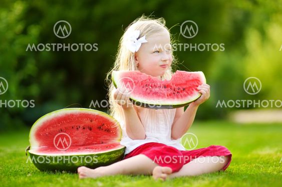 Funny little girl biting a slice of watermelon outdoors...