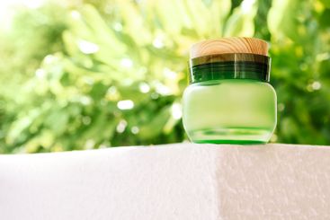 A close-up of a jar of cream made of green glass with a...