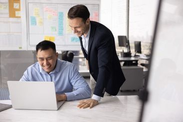 Happy male Caucasian boss checking positive Asian...