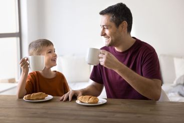 Father and son enjoying breakfast with croissants and...