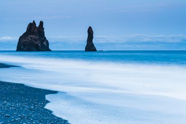 Coastal rocks rising from the blue waters of Iceland at...
