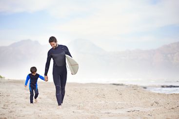 Surfboard, father and son holding hands on beach for...