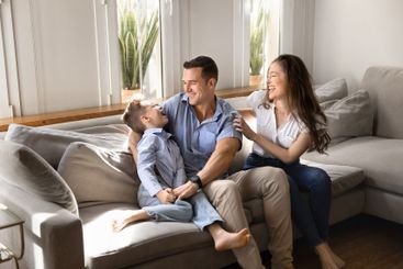 Happy young parents cuddling kid on home sofa