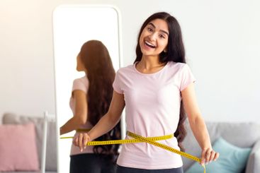 Indian woman measuring her waist with tape in front of...