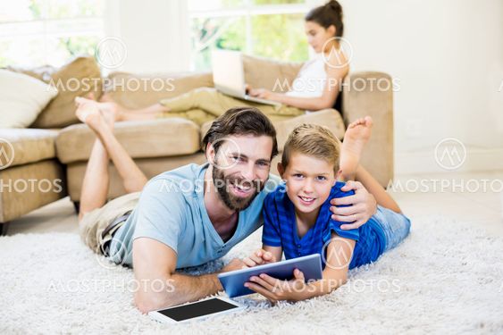 Portrait of father and son lying on rug and using digital...
