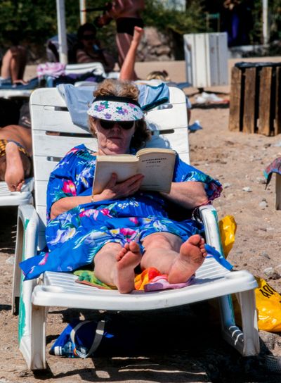 En dam ligger i en solstol på stranden och läser