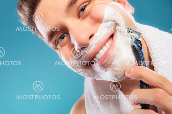 Happy man shaving using razor with cream foam.
