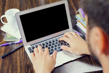 Person using laptop at a wooden table surrounded by...