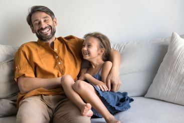 Middle-aged father laughing while tickling his little...
