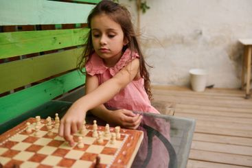 Young girl concentrating on a chess game outdoors,...