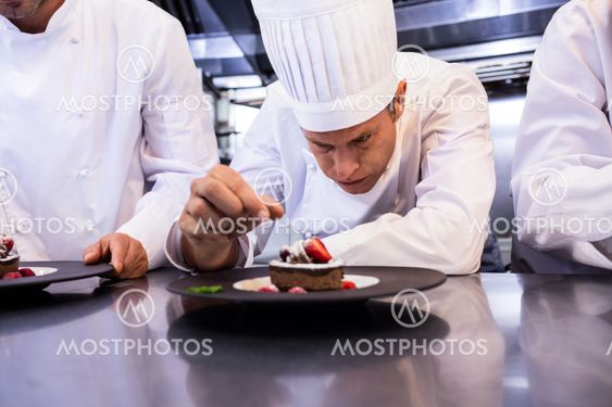 Male chef garnishing dessert plate on counter