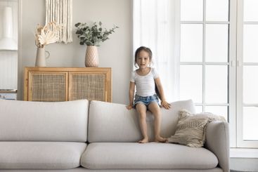 Little girl looking at camera sitting on back of sofa
