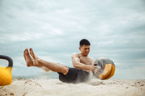 Young healthy man athlete doing squats at the beach