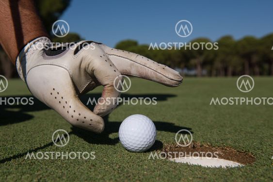 man's hand putting golf ball in hole