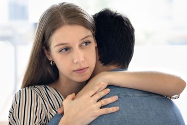 Thoughtful stressed beautiful young wife hugging husband