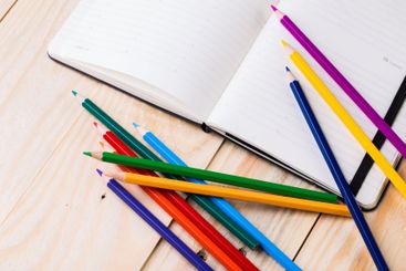 Colorful pencils scattered beside an open notebook on a...
