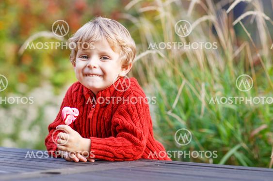 Funny little preschool boy sitting on a wall in late summer evening park, outdoors
