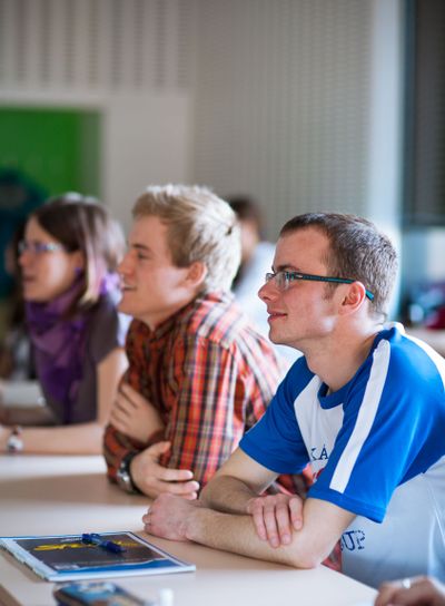 Handsome college student sitting in a classroom full of...