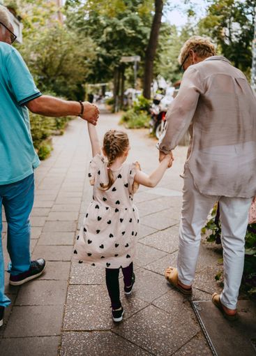 Grandparents holding hands of granddaughter while walking...