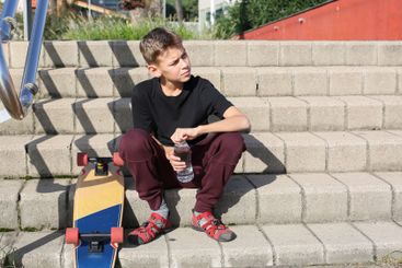Handsome teenager sitting with skateboard. Adolescent...