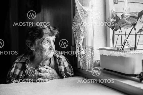 An elderly lady sits sadly near the window of his old...