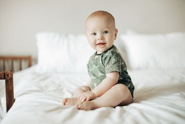 Cute, young and portrait of a baby on a bed sitting and...