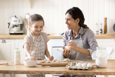 Happy laughing young mom teach little daughter to cook...