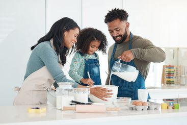 Parents, daughter and milk for baking in kitchen with...