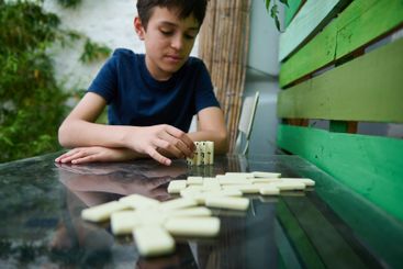 Young boy concentrating on a game of dominoes, playing...