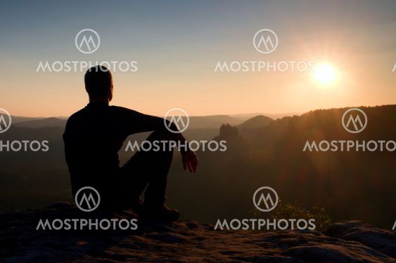 Hiker take relaxing on a rock and enjoying sunset at...