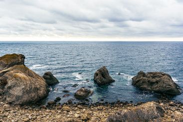 Rocky coastline with ocean waves and cloudy sky creates...