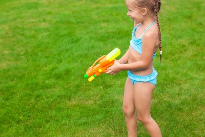 Little adorable girl playing with water gun outdoor in sunny summer day