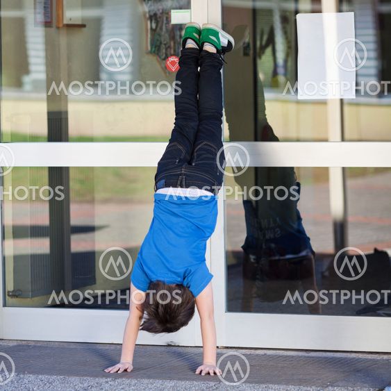 Student Doing Handstand Against Glass Wall In School