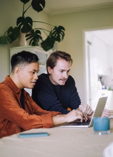Multiracial gay freelancers working on laptop while...