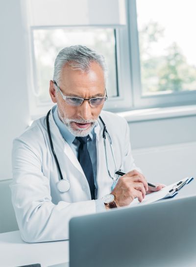 middle aged male doctor writing in clipboard and looking...