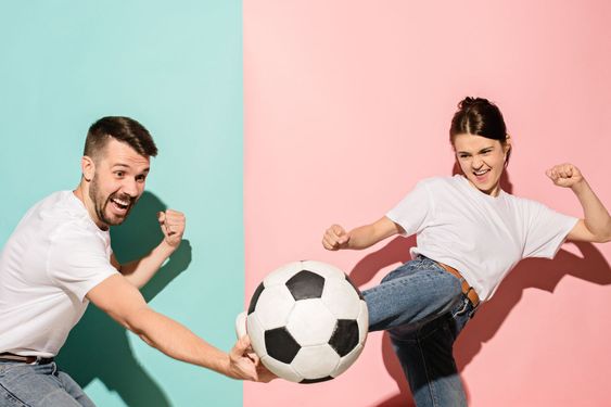 The young football fans plaing with ball on blue and pink...