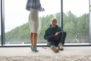 A blonde man sitting casually on the floor of a modern...