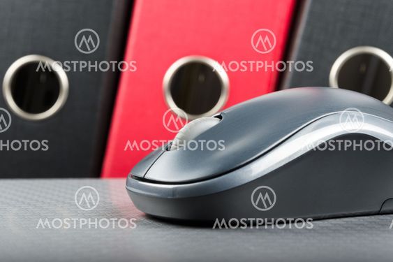 A wireless mouse placed on notebook and three folders in the background