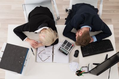 Two Businesspeople Sleeping On Desk In Office